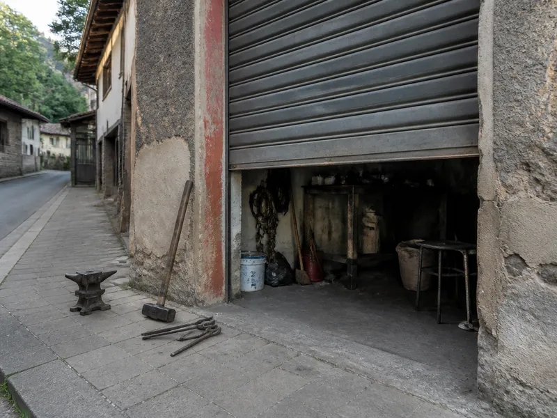 Persiana metálica de local entreabierta con herramientas en el suelo, sin rotulación comercial